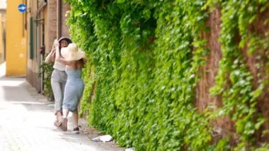 İtalyan şehrinde yürüyen ve yeşil duvarda dans eden iki gülen kadın