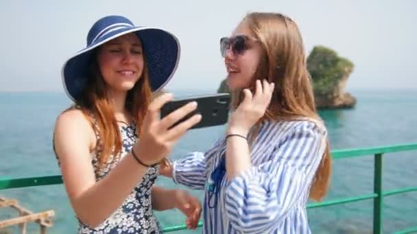 Две молодые женщины фотографируются на фоне моря — стоковое видео