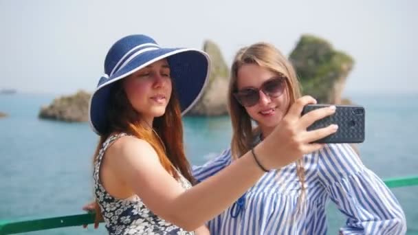 Dwie młode kobiety robią zdjęcia na telefon w tle morza — Wideo stockowe