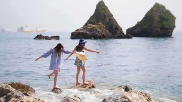 Δύο ελκυστικές γυναίκες διαμένουν και απολαμβάνουν σε μεγάλες πέτρες δίπλα στη θάλασσα. — Αρχείο Βίντεο