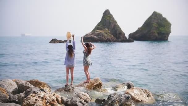 Zwei attraktive Frauen stehen auf einem großen Stein und winken mit den Händen — Stockvideo