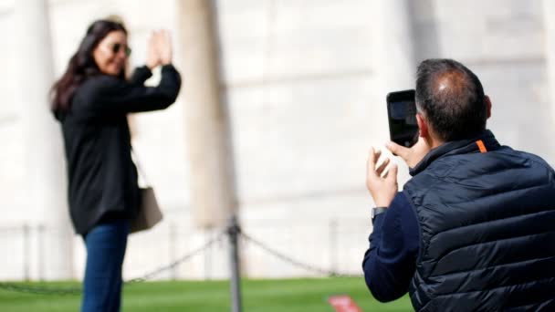 Мужчина фотографирует женщину с наклонной башней — стоковое видео