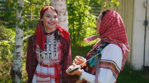 Duas jovens mulheres em russo vestido tradicional stand sob uma bétula árvore e dança . — Vídeo de Stock