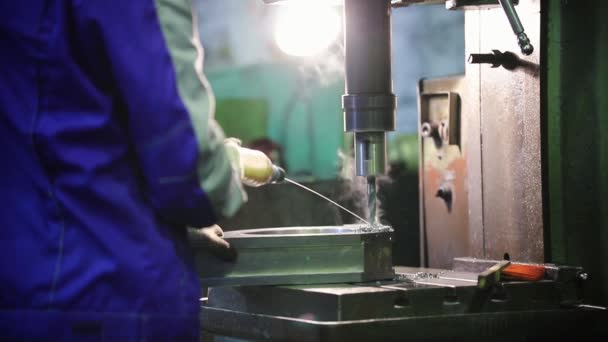 Um homem realiza trabalhos de perfuração em peças metálicas. Despeja fluido no material — Vídeo de Stock