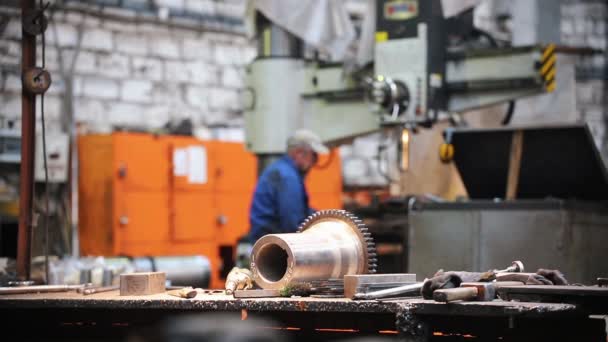 In der Fabrik auf dem Tisch liegen Metallteile und Werkzeuge - im Hintergrund arbeitet ein Mann an einer Werkzeugmaschine — Stockvideo