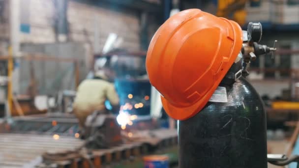 El casco rojo está en la bolsa de juntas para la soldadura - El hombre que trabaja en la soldadura en la distancia en la fábrica — Vídeos de Stock