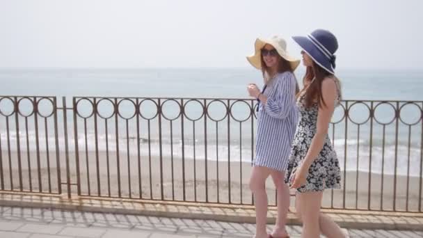 Dos mujeres atractivas en vestidos y panamá, caminan por el paseo marítimo en Sorrento — Vídeo de stock