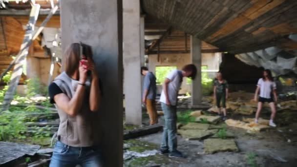 Выжившая женщина с пистолетом прячется за колонной от зомби в заброшенном здании — стоковое видео
