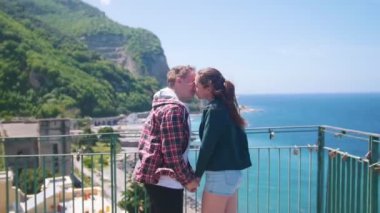 Mutlu genç çift denize yakın tatil kasabasının bir arka plan üzerinde bir gözlem güvertesinde ayakta ve öpücük