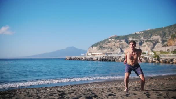 Um jovem a jogar frisbee na praia. Saltar e pegar o disco — Vídeo de Stock