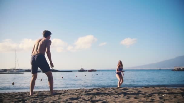 Un joven jugando frisbee en la playa con su novia — Vídeo de stock