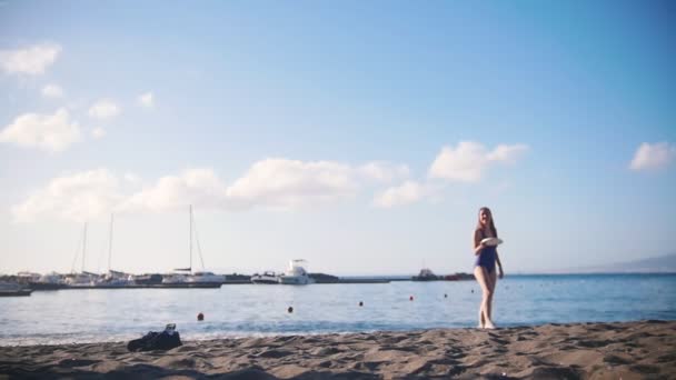 Un joven jugando al frisbee en la playa con su novia. Coger el disco y caer en la arena — Vídeo de stock