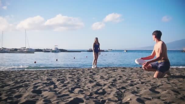 Молодой человек играет во фрисби на пляже со своей девушкой. Бросаю ей диск. — стоковое видео