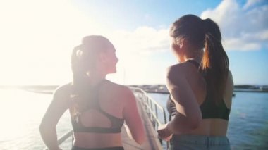 Güneşli bir günde köprüde deniz limanına doğru koşan spor kıyafetli iki genç kadın