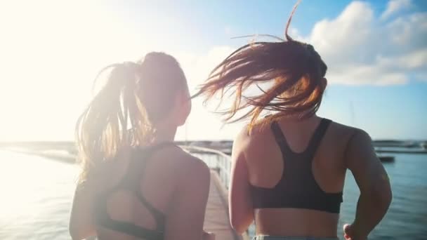 Két fiatal nő kocogni a hídon felé a tengeri kikötő napsütéses napon — Stock videók