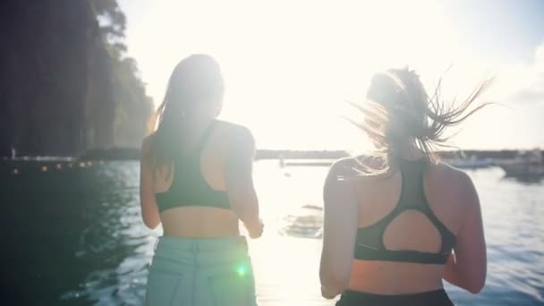 Две молодые женщины с хвостиками бегают по мосту — стоковое видео