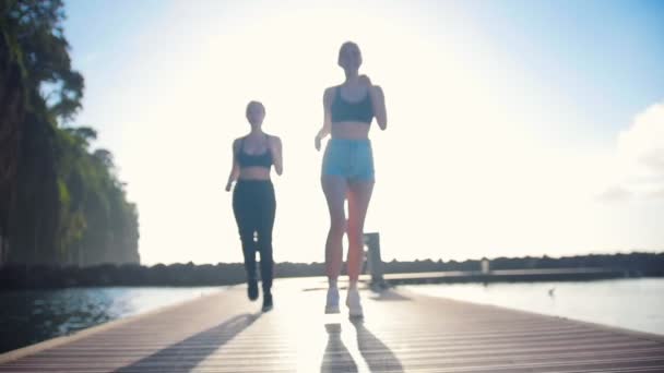 Dos jóvenes corriendo en el puente sobre el mar — Vídeo de stock