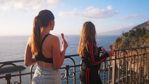 Dos mujeres jóvenes de pie en un muelle de mar y comer helado después de la formación y mirando a su alrededor — Vídeos de Stock