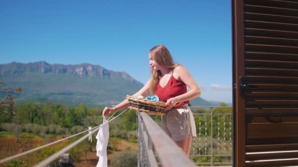 Een jonge vrouw hangen natte kleren op het touw — Stockvideo