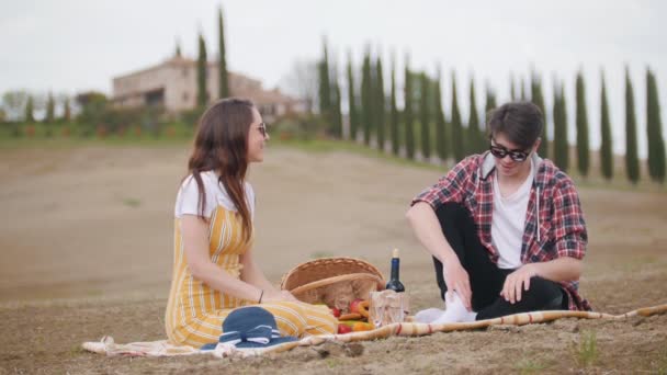 Ett ungt talande par sitter på täcket med en picknick på bakgrunden av cypress träd — Stockvideo