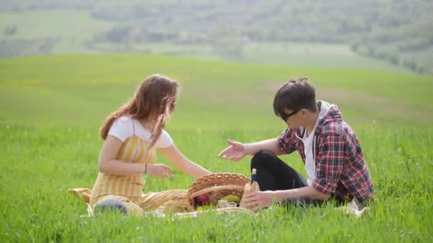A young couple in bright clothes sitting on a bright green meadow and looking what is in the pottle — Stock Video