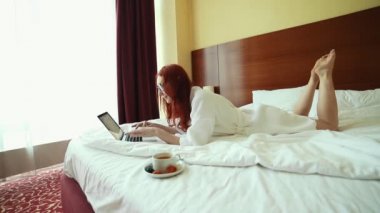 Bir zencefil kadın yatakta yatan ve bir dizüstü bilgisayar ile çalışan - çay içmek