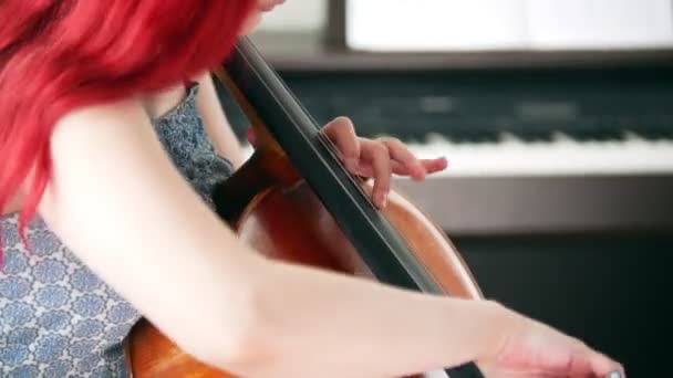 Uma mulher com cabelo rosa tocando emocionalmente o violoncelo na sala — Vídeo de Stock