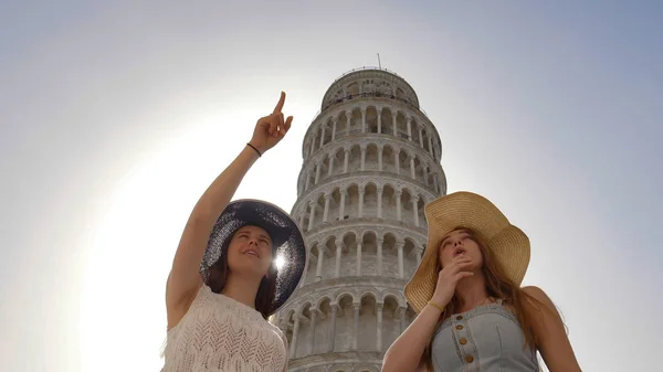 Dos mujeres atractivas se muestran algo en el fondo de la Torre Inclinada . —  Fotos de Stock