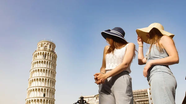 Dos mujeres jóvenes en panamas de pie sobre un fondo de la Torre Inclinada y mirándola —  Fotos de Stock