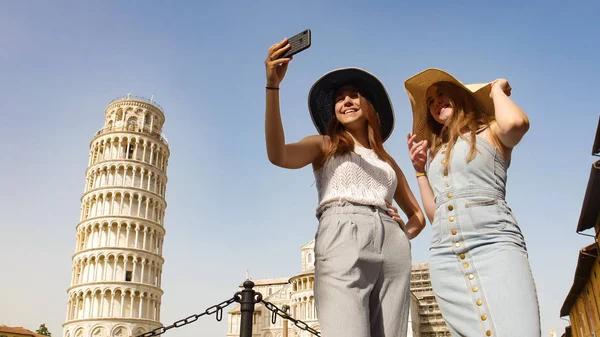 Dos mujeres jóvenes se toman un selfie en el fondo de la Torre Inclinada . —  Fotos de Stock