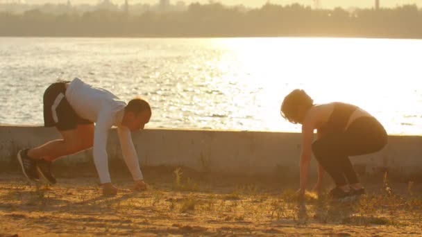Man en vrouw voert push-ups met de sprongen op de waterkant tijdens zonsondergang — Stockvideo