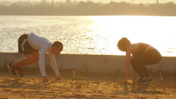 Man och kvinna utför armhävningar med hopp på vattnet under solnedgången — Stockvideo