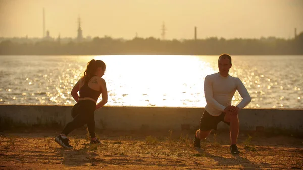 Un hombre y una mujer amasando los músculos de las piernas antes del entrenamiento en el paseo marítimo —  Fotos de Stock
