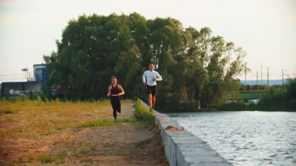 Férfi és nő fut a párkányon a rakparton, háttérben az erdő — Stock videók
