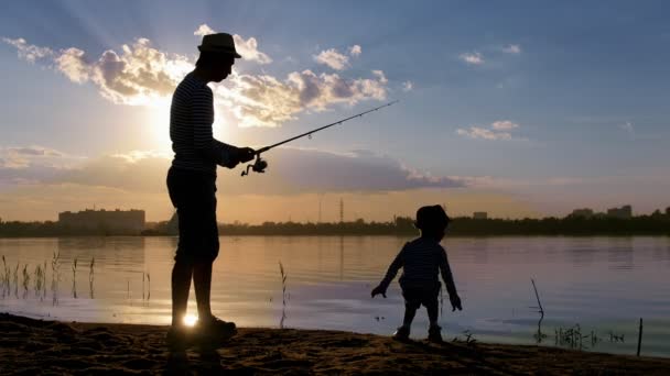 En far och hans son i par kläder som fiskar i solnedgången — Stockvideo