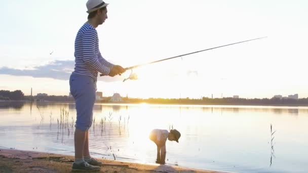 Un père et son fils en train de pêcher ensemble - un homme tenant la canne et pêchant et son fils marchant sur la plage - coucher de soleil — Video