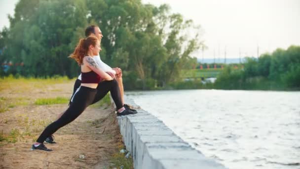 Hombre y mujer estirando los músculos de las piernas apoyando sus pies en el hormigón en el terraplén — Vídeo de stock