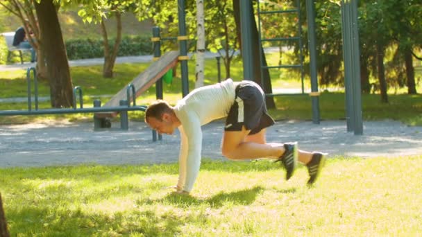 Hombre atlético culturista hace embestidas, teniendo el énfasis en mentir. en un campo verde en medio de un parque — Vídeos de Stock