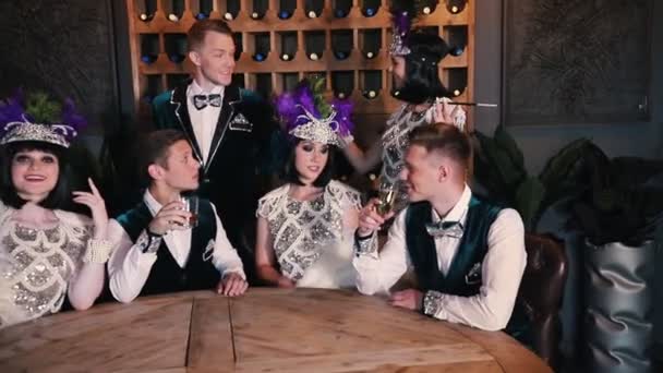 Themenparty - junge Leute in glitzernden Kleidern sitzen hinterm Tisch und unterhalten sich beim Trinken — Stockvideo