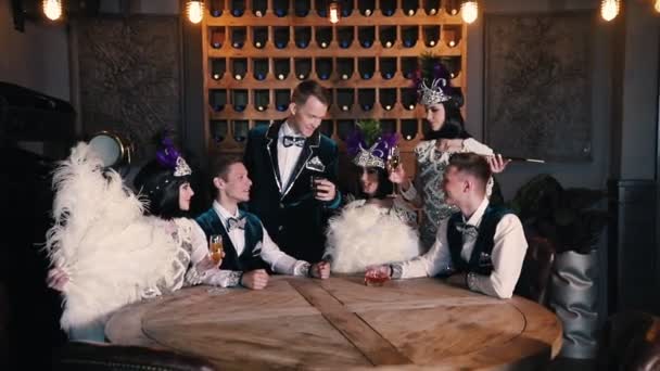 Tema Party-människor i glittrande kläder sitter bakom bordet och pratar-en man i mitten höjer ett glas dricka upp — Stockvideo