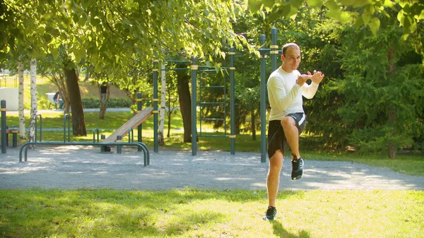 En atletisk man värmer upp benen med grundläggande övningar i parken — Stockfoto