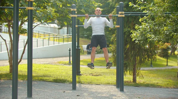 En atletisk man utför pull ups på bat på sporten marken — Stockfoto