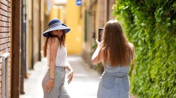 Két fiatal nő sétál a sikátorokban-egyikük pózol a fotó — Stock Fotó