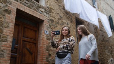 İki genç kadın şehirde yürüyor ve selfie çekiyor