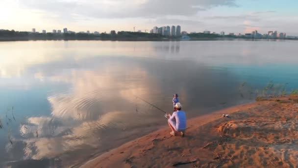 Un padre y su hijo en la pesca juntos de pie en la costa del lago al atardecer en el centro de la ciudad — Vídeos de Stock