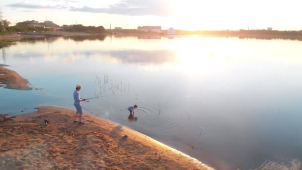 Een vader en zijn zoon om samen te vissen-staan aan de kust van het meer bij zonsondergang — Stockvideo