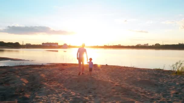 Lazer familiar - Um pai e seu filho em roupas de casal andando na pesca na costa do rio de mãos dadas - pôr do sol — Vídeo de Stock