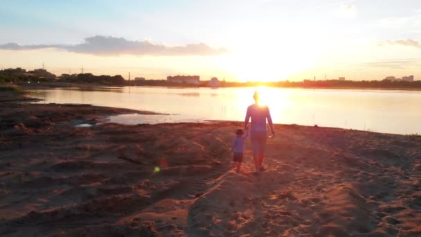 Lazer familiar - Um pai e seu filho em roupas de casal andando na pesca na praia do rio de mãos dadas em um fundo do pôr do sol — Vídeo de Stock