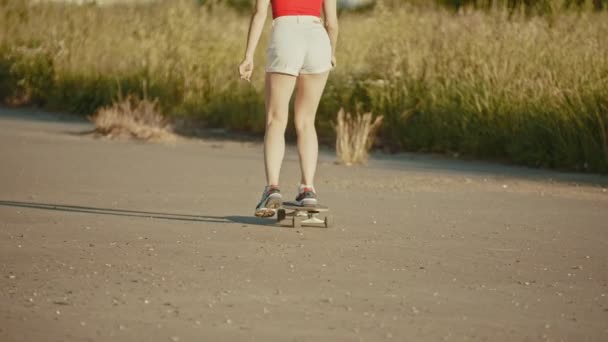Молодая женщина с красивыми ногами катается на скейтборде на фоне высокой травы — стоковое видео