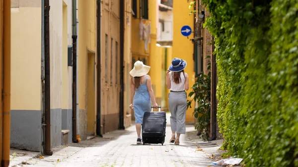 Dos mujeres caminando bajan por el carril. Uno de ellos llevando una maleta . —  Fotos de Stock